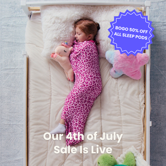 child-sleeping-on-a-cream-bed-sheet-while-wearing-a-pink-leopard-print-junior-sleep-pod-and-holding-a-plush-unicorn-badges-say-bogo-50-off-all-sleep-pods-and-our-4th-of-july-sale-is-live