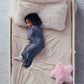 Child sleeping on a cream bed sheet while wearing a navy ribbed Junior Sleep Pod with a pink star pillow nearby.