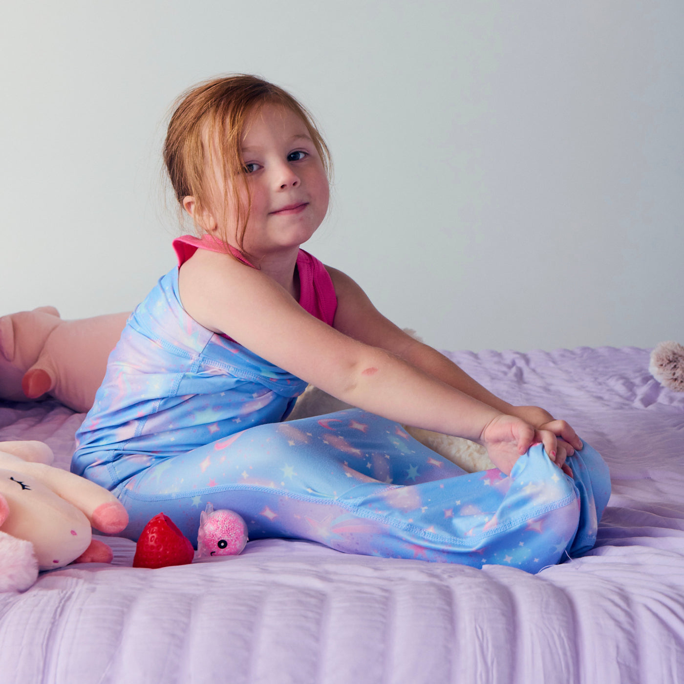 Child sitting on a bed while wearing a blue star print Junior Sleep Pod and stretching the fabric over their feet.