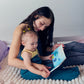Adult reading with a young child on a bed while both are wrapped in turquoise and graphite color Sleep Pods.