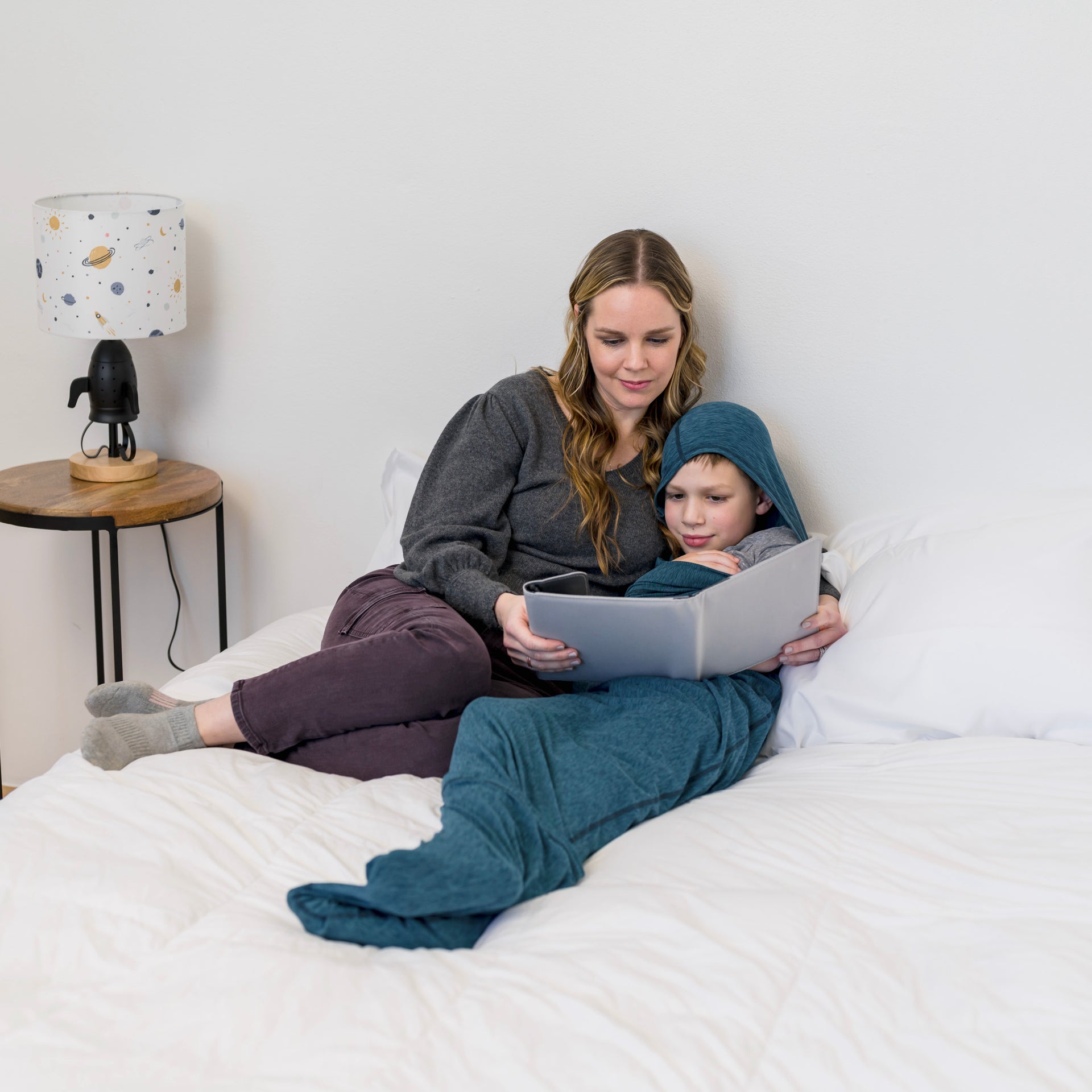 mother reading book to child laying a sleep pod in bed