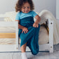 Child sitting on a low bed while wearing a turquoise Junior Sleep Pod and pulling the fabric over their legs.