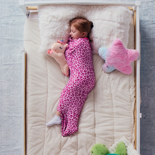 child-sleeping-on-a-cream-bed-sheet-while-wearing-a-pink-leopard-print-junior-sleep-pod-and-holding-a-plush-unicorn