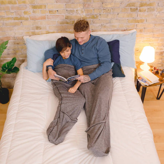 father-and-son-laying-in-bed-wearing-sleep-pods-reading-a-book